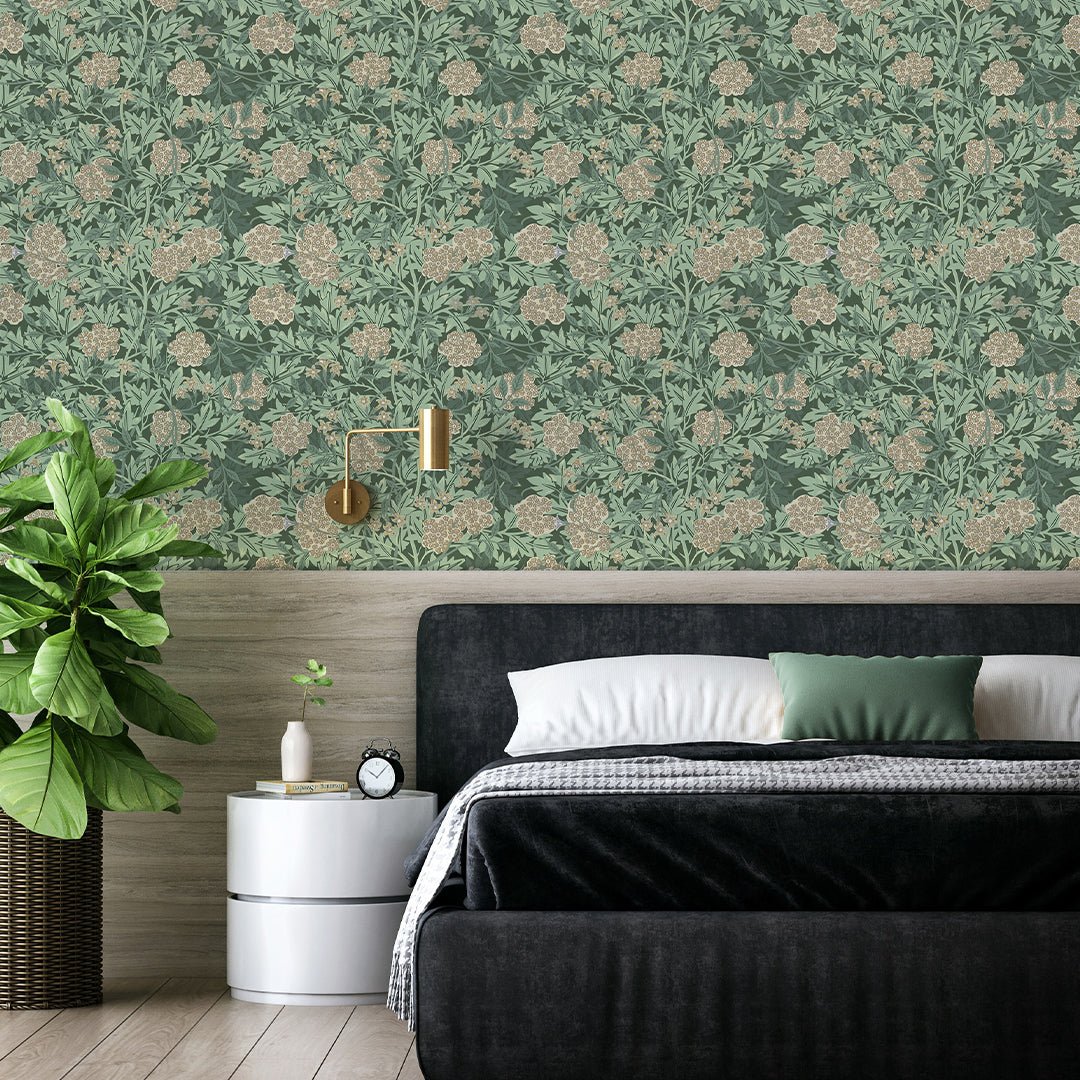 Green floral peel-and-stick wallpaper above light wood paneling, black upholstered bed, gold wall sconce and potted plant