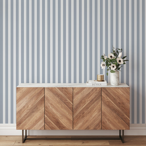 Coastal wallpaper in muted dusty blue and white with refined vertical stripes, creating a clean backdrop for nurseries and elegant modern interiors.