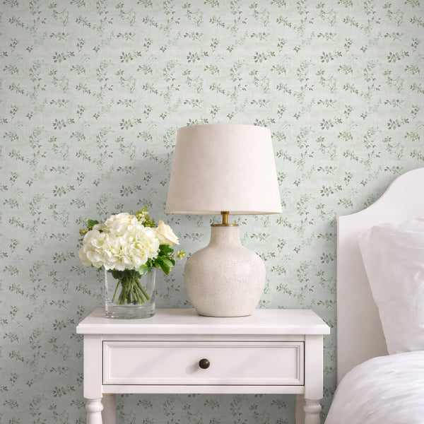Floral vine wallpaper featuring sage green vine sprigs and tiny leaf clusters on a pale ground with a linen texture. The open, low-density repeat adds a soft botanical touch, suitable for hallways or home offices. This high-quality removable wallpaper is easy to apply and reposition, offering a temporary decor solution.