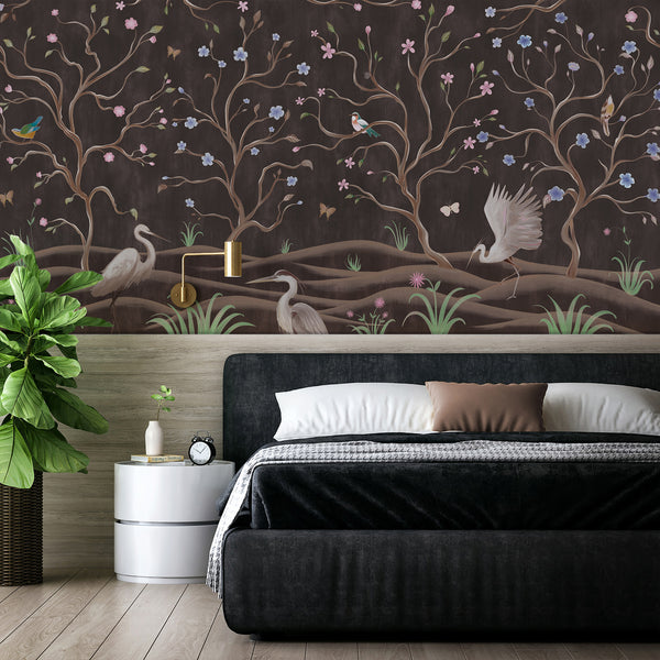 Dark brown floral wallpaper featuring elegant flowering trees, heron birds, butterflies and botanical details for a bedroom or living room.