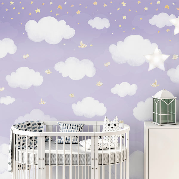 Watercolor cloud wall mural with fluffy white clouds, tiny cream birds and scattered yellow stars on a pastel lavender background for a baby nursery.