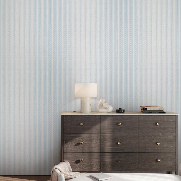 Pastel blue botanical wallpaper featuring vertical floral stripes, white line art flowers, and subtle texture for cottagecore nursery walls or bedrooms.