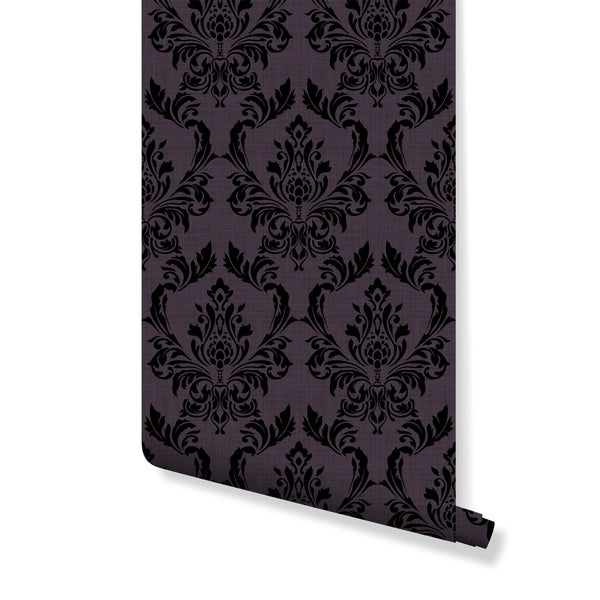 Purple Damask wallpaper featuring bold black ornamental motifs on a muted purple background with a woven texture. Perfect for gothic or eclectic interiors, this pre-pasted wallpaper creates dramatic contrast in bedrooms or dining areas. Made in the USA, it's ideal for those seeking rich color and pattern with eco-friendly, high-quality materials.