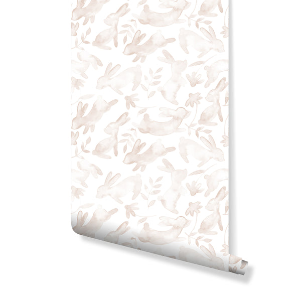 Warm beige bunny silhouettes with botanical sprigs on a white ground create a soothing nursery wallpaper. Ideal for a child's room or a modern Scandinavian accent wall, this removable peel and stick wallpaper offers an airy watercolor effect. Made in the USA with eco-friendly materials, it's perfect for renters seeking temporary yet stylish home decor.