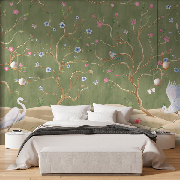 Chinoiserie wall mural with white herons, delicate pink and blue flowers, twisting branches and birds against a soft sage green background.
