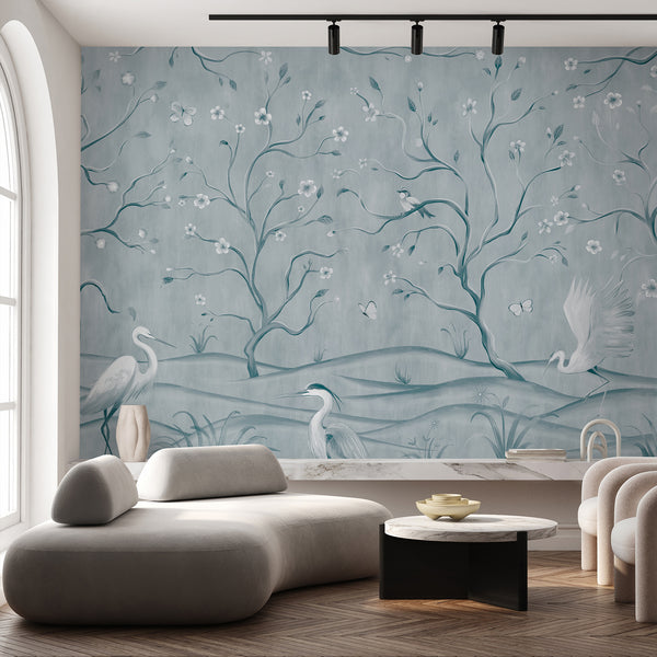 Light blue chinoiserie wallpaper with elegant herons, flowering tree branches, small birds and butterflies in a soft watercolor landscape.