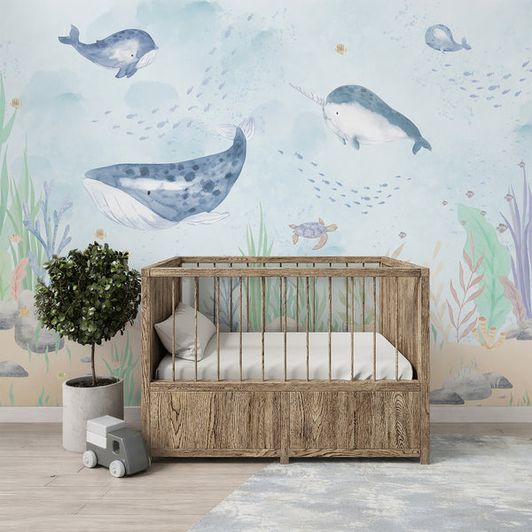 Blue whale nursery wall mural featuring watercolor whales, narwhal, turtle, tiny fish, coral reefs, rocks, and pastel underwater plants.