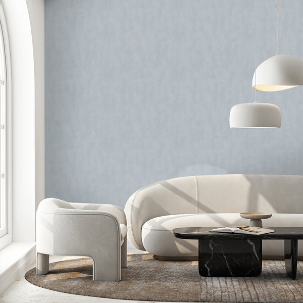 Subtle pale blue wallcovering with plaster-like texture and gentle tonal shifts, offering understated depth for calm bedrooms or home offices.