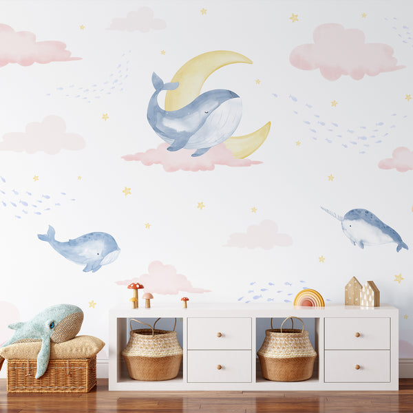 Whimsical whale wallpaper featuring soft blue watercolor whales, a narwhal, blush pink clouds, yellow moon and stars on a white background.