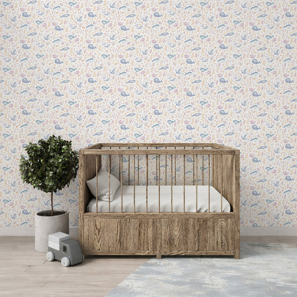 Whimsical whale wallpaper with watercolor marine animals, coral reefs, shells, and ocean plants in muted blue, blush pink, peach, and beige tones.