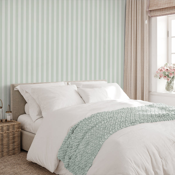 Removable wallpaper in pale sage green and white with alternating broad stripes and narrow pinstripe details for a fresh bedroom accent wall.