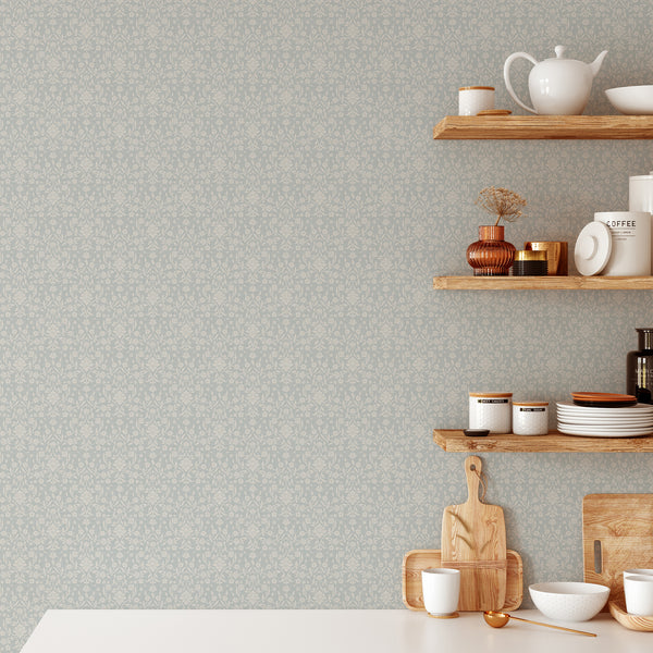 Vintage farmhouse damask wallpaper featuring cream floral silhouettes and elegant winding vines against a dusty blue textured background for bedroom walls.