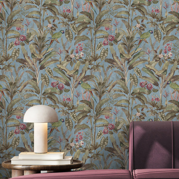 Tropical bird wallpaper with green parrots, muted pink blossoms and dense vintage botanical foliage on a textured dusty blue background.