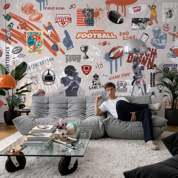 Bold football-themed wall mural with graffiti-style illustrations and energetic textures, perfect for a teen's bedroom or sports-themed playroom. The removable wall mural features players, footballs, and paint drips in rust orange, navy blue, and black tones, creating a lively and contemporary interior design.