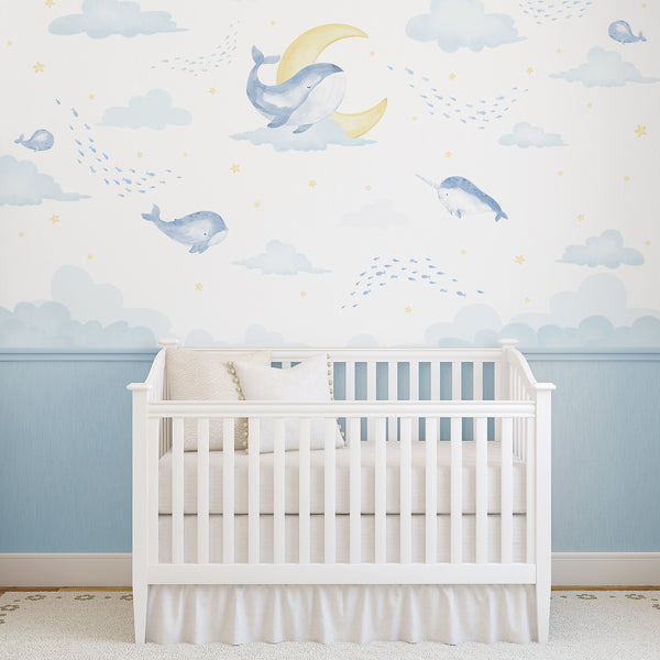 Watercolor whale nursery wallpaper featuring soft blue whales, a narwhal, tiny fish, pale clouds, yellow moons and stars on a white background.