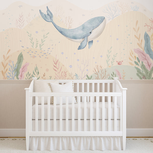 Ocean nursery wallpaper featuring a watercolor blue whale surrounded by small fish, bubbles, coral reefs, seaweed, and soft pastel underwater scenery.