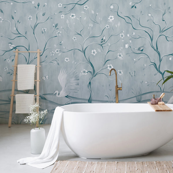 Vintage chinoiserie wall mural with white herons, blue botanical branches, tiny blossoms and birds against a textured light blue background.
