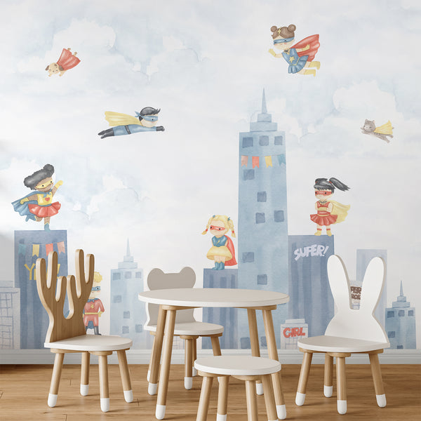 Kids room superhero wall mural with watercolor children in red, blue, and yellow costumes flying over a pastel city skyline and cloudy sky.