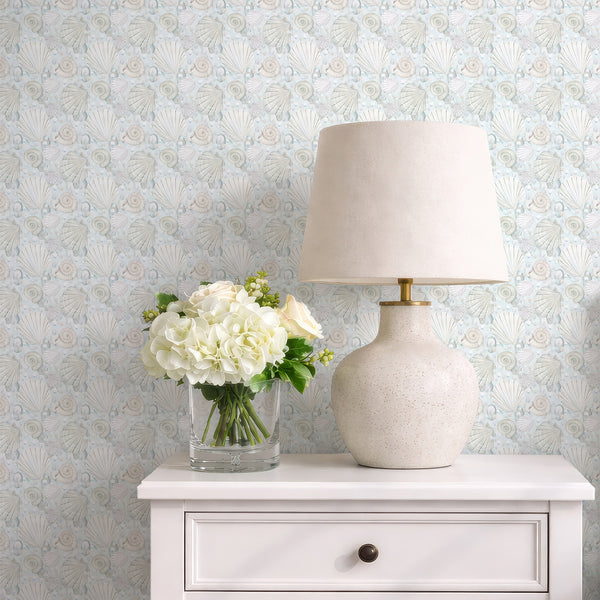 Nautical wallpaper with watercolor seashells, spiral shells, and floating pearl accents in muted blue and sandy neutral tones.