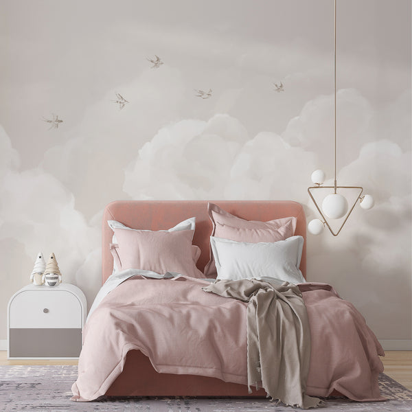 Neutral cloud wallpaper featuring warm beige tones, fluffy white clouds and graceful flying birds for a soft gender neutral nursery or bedroom accent wall.