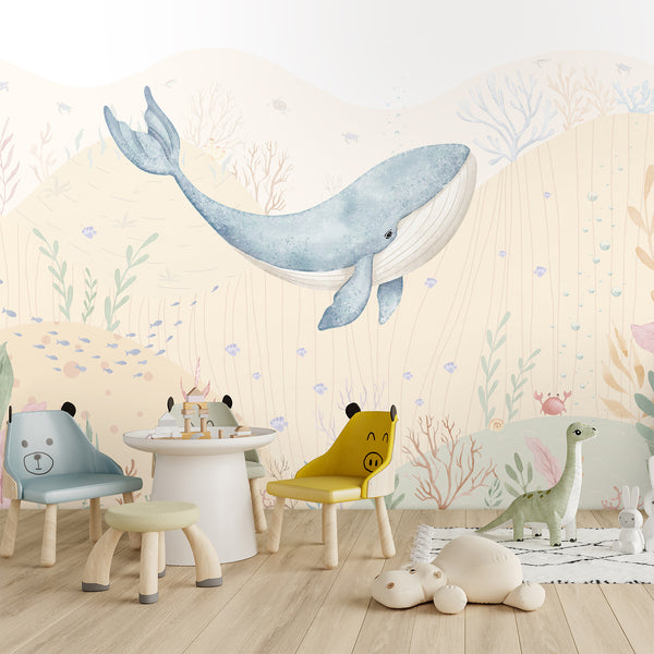 Underwater nursery wall mural with a gentle blue whale swimming through pale beige ocean hills, colorful coral, tiny fish, and sea plants.