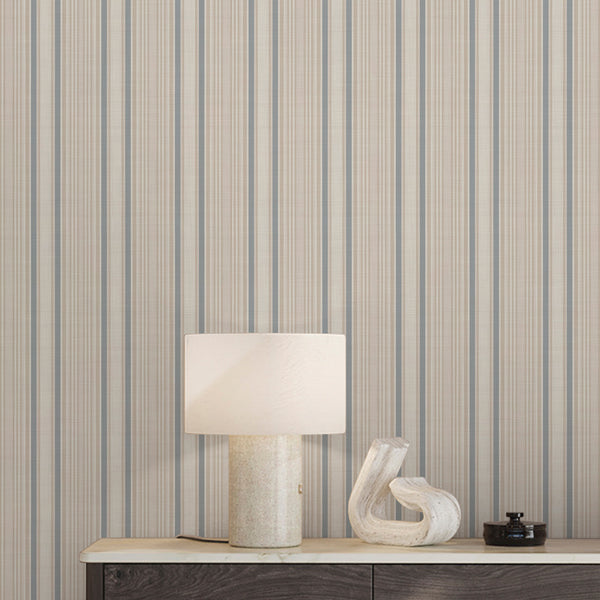 Coastal cottage wallpaper featuring alternating beige and dusty blue ticking stripes with subtle textile-inspired texture, ideal for relaxed beach house interiors.
