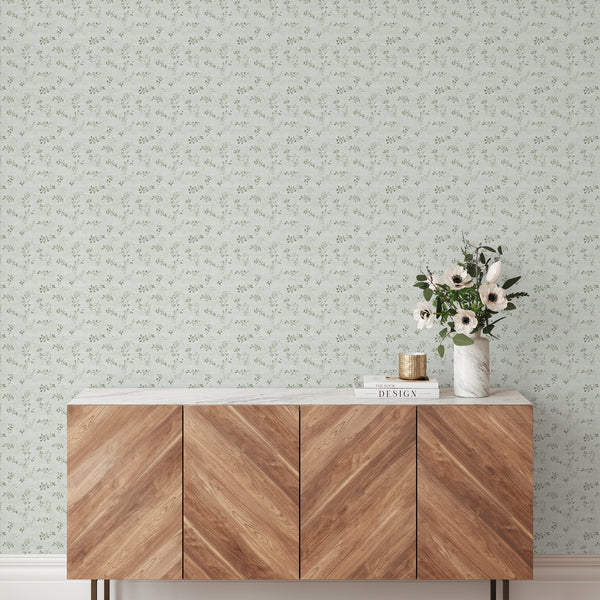 Green floral vine wallpaper featuring scattered vine sprigs and leaf clusters on a pale, linen-textured ground. The open repeat adds a soft botanical touch, suitable for home offices or hallways. This pre-pasted wallpaper offers easy application and is perfect for decorators seeking a light, vintage-inspired design.