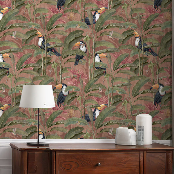 Dusty pink tropical toucan wallpaper featuring exotic black and white birds with orange beaks among olive green banana leaves and lush jungle foliage.