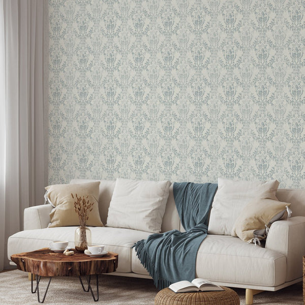 A detailed view of Light Blue Rococo wallpaper showcases faded ornamental motifs on a warm ivory ground. The weathered, fabric-like finish is perfect for a classic accent wall, offering easy application with its pre-pasted design.