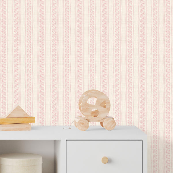 Cottagecore wallpaper in blush pink with white textured background, graceful floral line drawings, and decorative stripe details for cozy nursery decor.
