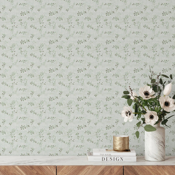 Green floral vine wallpaper featuring fine vine sprigs and leaf clusters in sage green on a pale, textured ground. The gentle diagonal and vertical rhythms create a cozy, timeless aesthetic, suitable for hallways or home offices. This removable peel and stick wallpaper is eco-friendly, made in the USA, and perfect for renters.