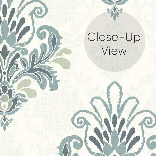 Close up of blue and ivory peel and stick wallpaper featuring repeating damask medallions with intricate floral shapes, graceful curves and a softly textured finish.