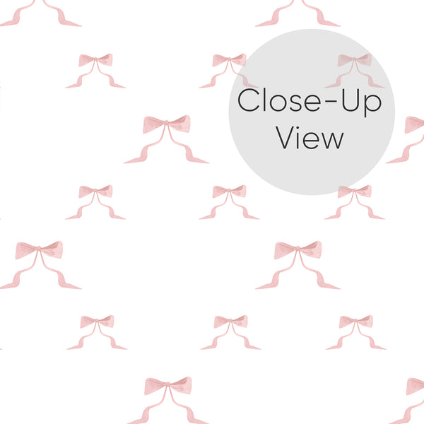 Close up of blush pink bow wallpaper with hand-painted ribbon details and airy white space, ideal for a toddler room or nursery accent wall.