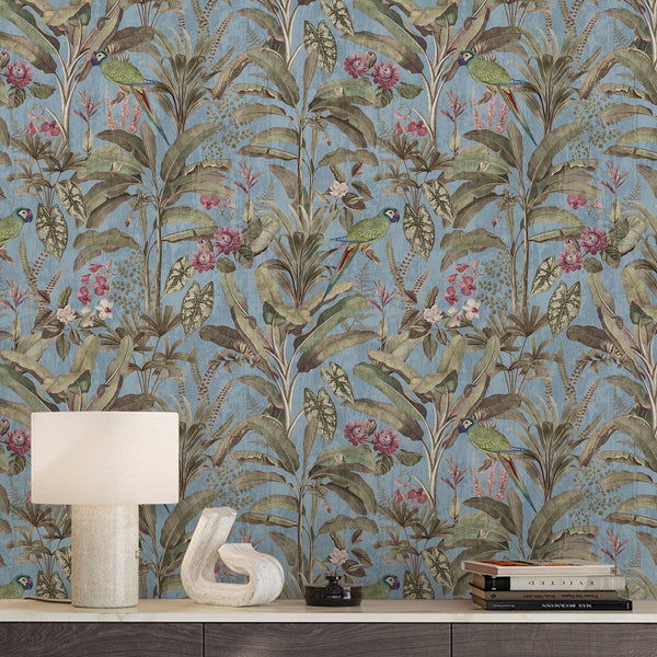 Blue tropical wallpaper featuring green parrots, muted pink flowers and lush botanical foliage in a detailed vintage jungle illustration style.