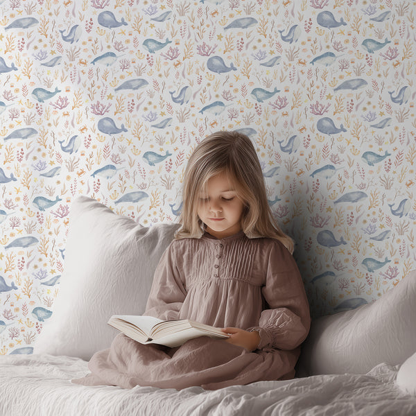 Watercolor ocean nursery wallpaper with a smiling blue whale, colorful coral branches, seashells, starfish, and small tropical fish on white.