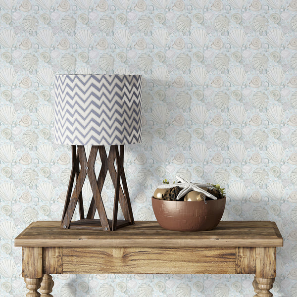 Coastal seashell wallpaper featuring watercolor scallop shells, spiral shells, pearls, and soft blue ocean tones on a light neutral background.