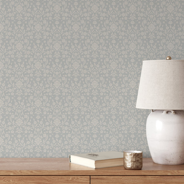 Dusty blue floral wallpaper featuring large cream flowers, flowing botanical vines and decorative leaves on a muted blue background with woven texture in damask style.